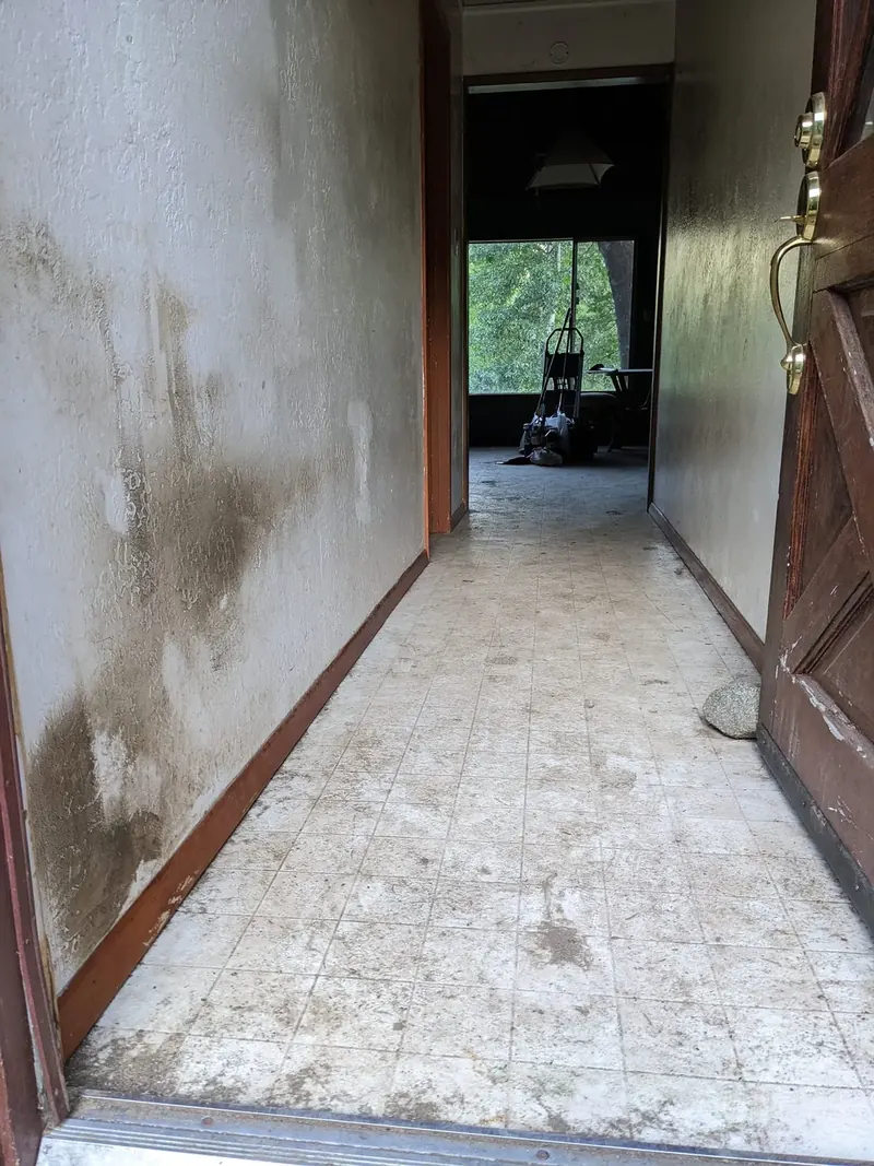 Entry hallway before cleaning, with dark staining across the textured wall and a soiled tile floor.
