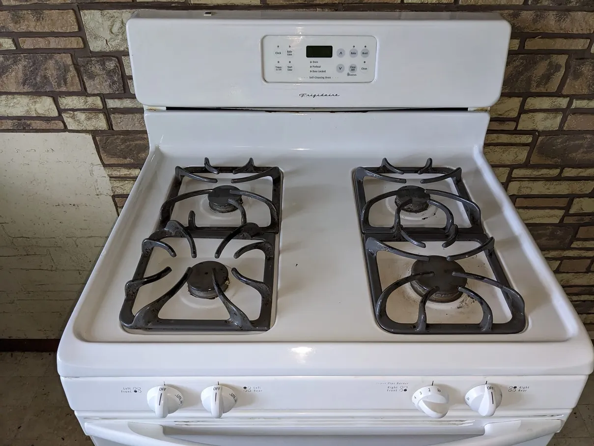 The same gas range after cleaning, with a bright white cooktop and degreased burner grates.