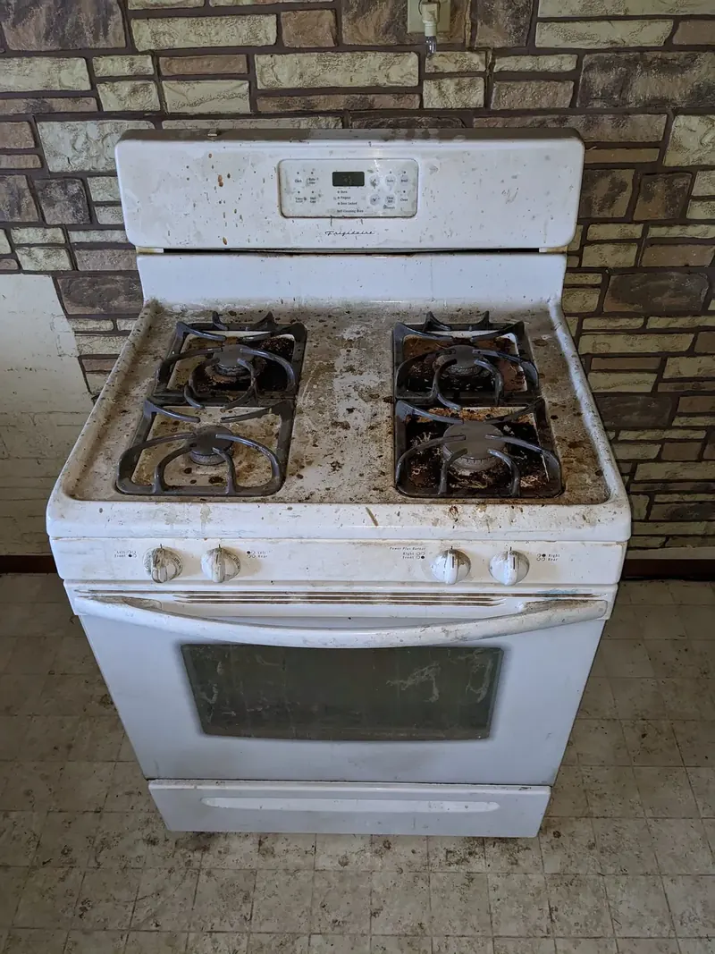 Gas range before cleaning, covered in baked-on food debris across the cooktop, grates and control panel.
